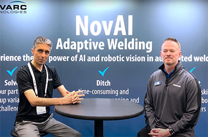 Two men sitting at a round table in front of a backdrop displaying "NovAI Adaptive Welding." They are representing AVARC Technologies at an event, possibly discussing AI and robotic vision in welding.