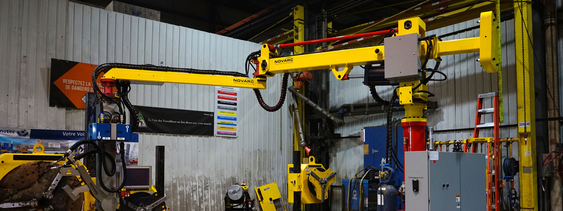 Industrial robotic arms in a factory setting, featuring bright yellow machinery with cables and control panels.