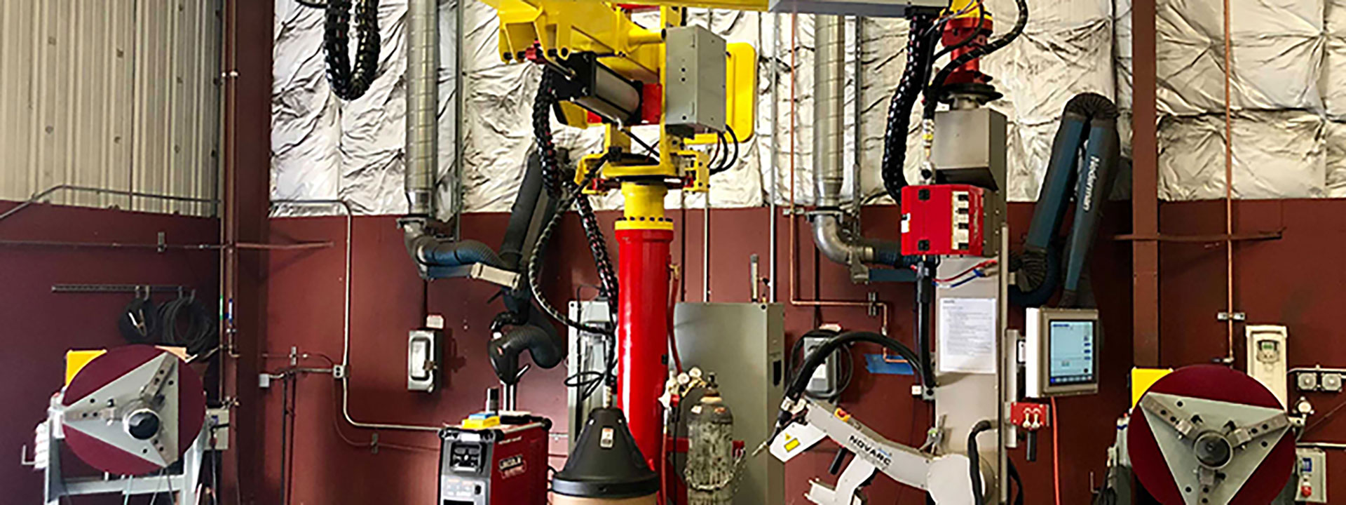 A factory setting with industrial machines, including robots with red and yellow arms, control panels, and various cables.