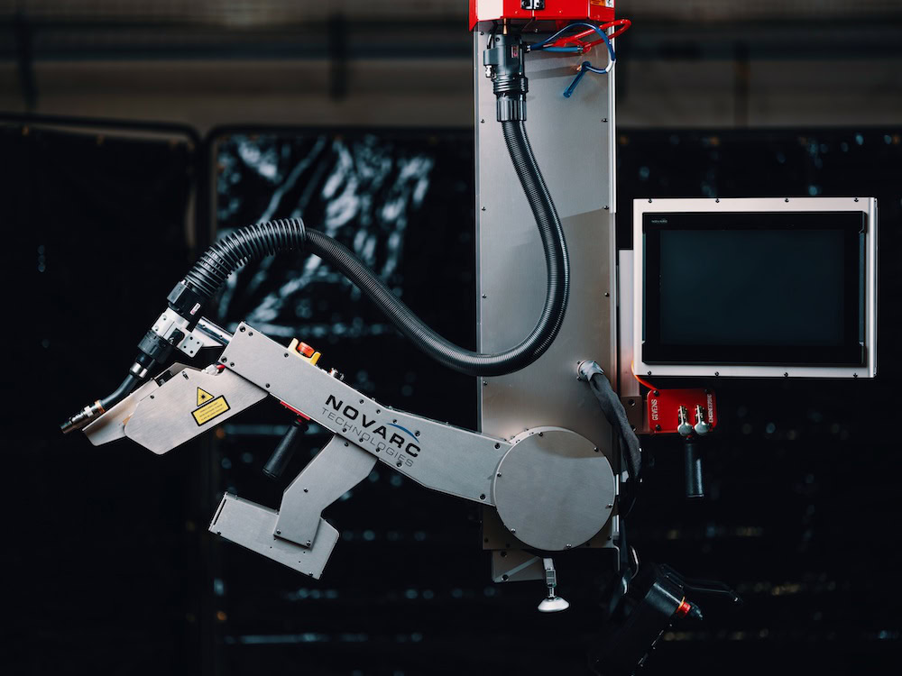 A robotic welding arm with a flexible hose and control panel. The machine is mounted vertically with a display screen on the right side. The arm is metallic and industrial in design, positioned against a dark, blurred background.