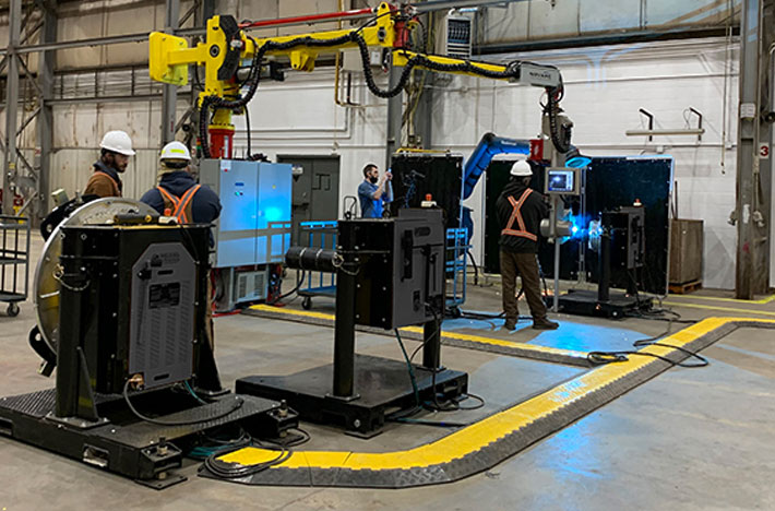 People wearing safety gear work in an industrial setting with robotic machinery and equipment.