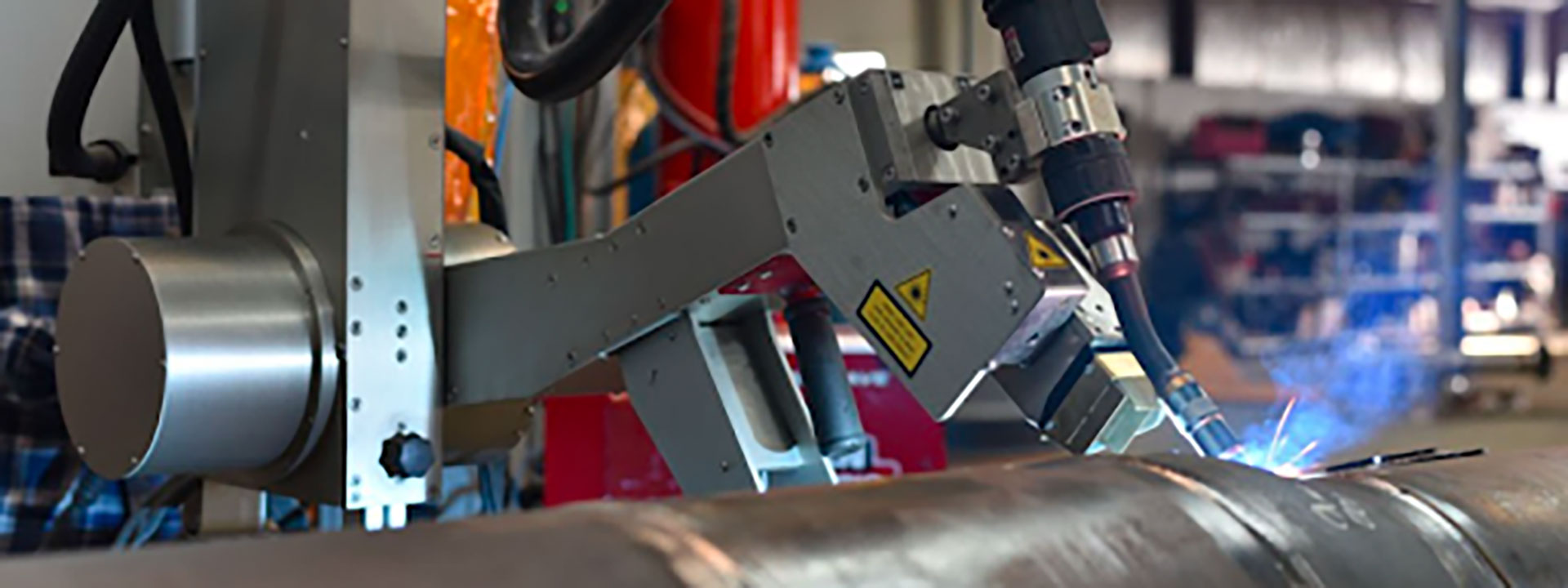 A robotic arm is performing welding on a metal pipe in an industrial setting, producing bright sparks.