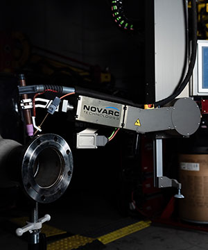 A robotic arm labeled "Novarc Technologies" is shown welding a round metal flange in a dark industrial setting.