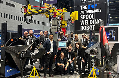 A group of people poses around an autonomous spool welding robot in a technology exhibition.