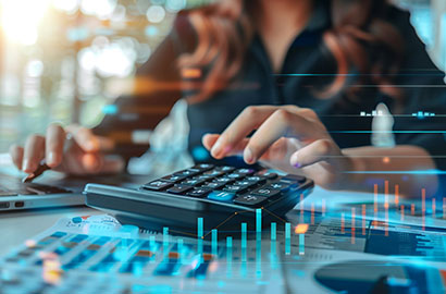 A person using a calculator and laptop, surrounded by financial graphs and documents.