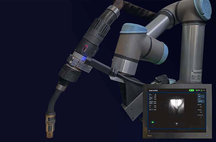 A robotic welding arm with a nozzle is positioned next to a display screen showing welding parameters and an image of a weld in progress.