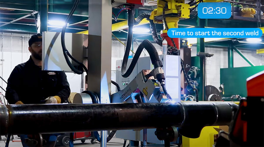 A worker operates welding machinery in an industrial setting, preparing a pipe. A digital timer reads "02:30" with text indicating "Time to start the second weld" in a blue overlay.