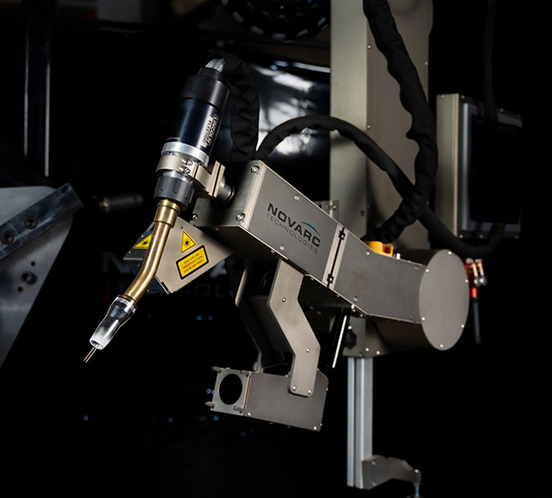 A close-up of an industrial robotic welding arm with metallic components and a precision nozzle. The background is dark, highlighting the Novarc Technologies branding on the arm.