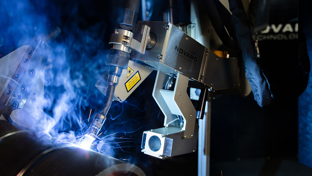 A robotic arm engaged in welding, emitting bright sparks and surrounded by smoke. The metallic machinery showcases precise engineering.