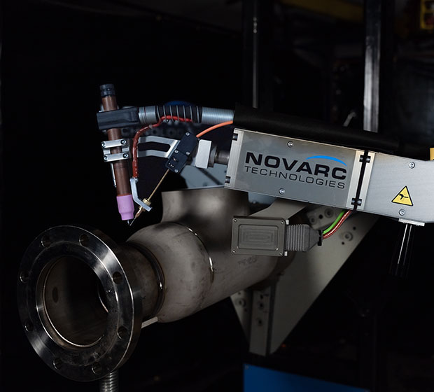 A robotic welding arm labeled "Novarc Technologies" performing welding on a cylindrical metal pipe with a flange.