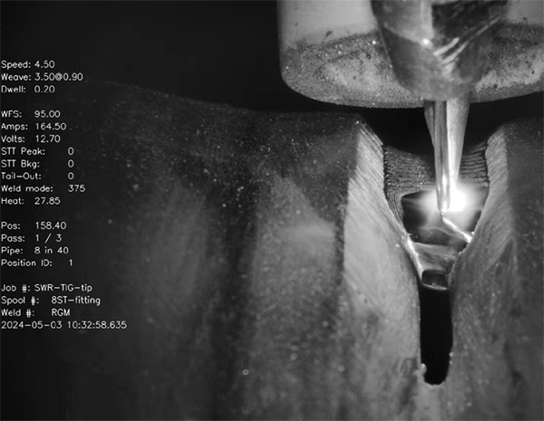 Close-up of a welding process with visible sparks and a welding torch. On-screen data displays settings like speed, amps, and position.